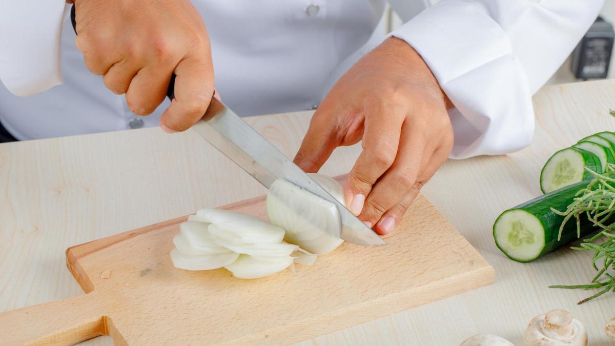 Репчатый лук режут ножом на разделочной доске