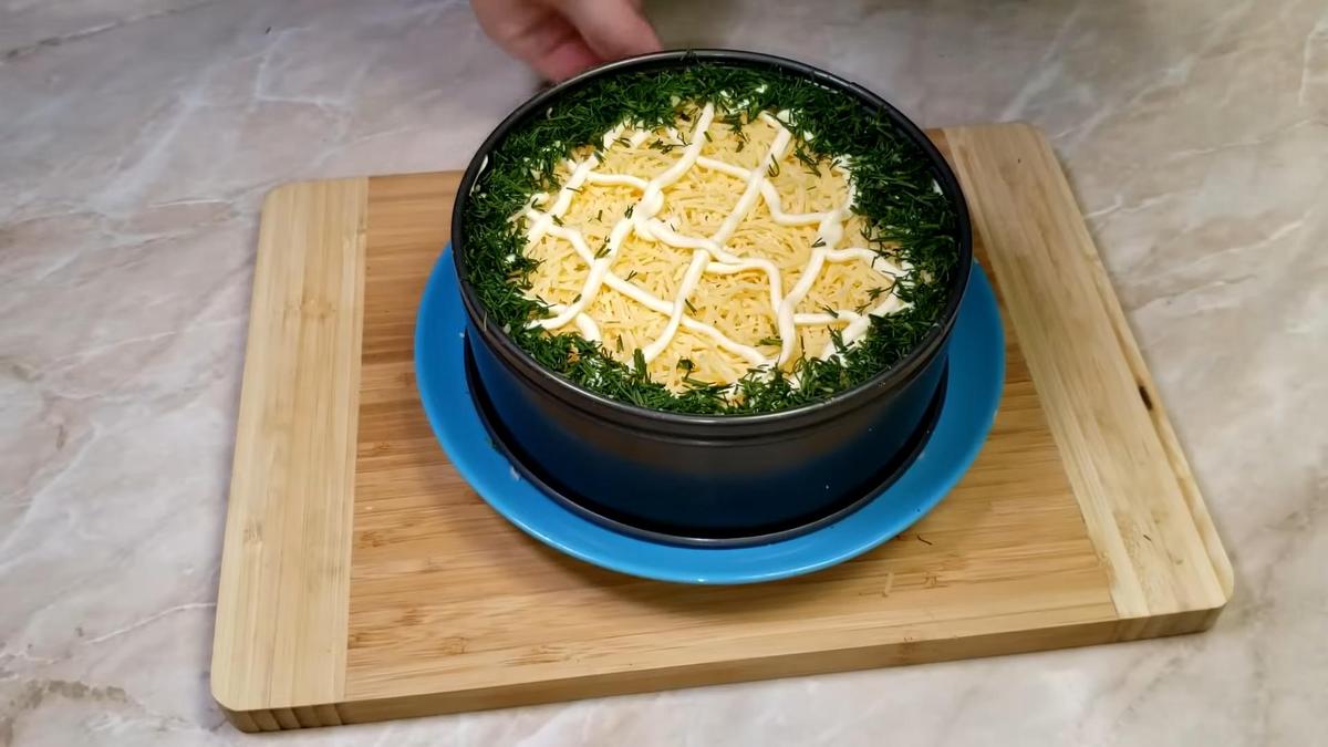 Салат в формовочном кольце, посыпанный сыром и зеленью, с сеточкой из майонеза