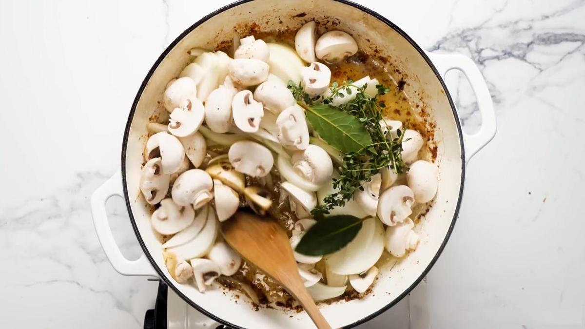 На сковороде жарят лук, шампиньоны с добавлением тимьяна и лаврового листа