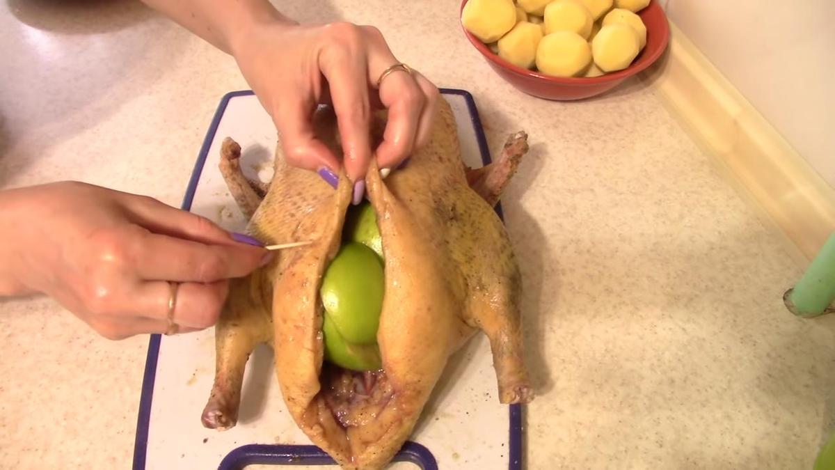 Женские руки скалывают шов на фаршированной утке зубочистками