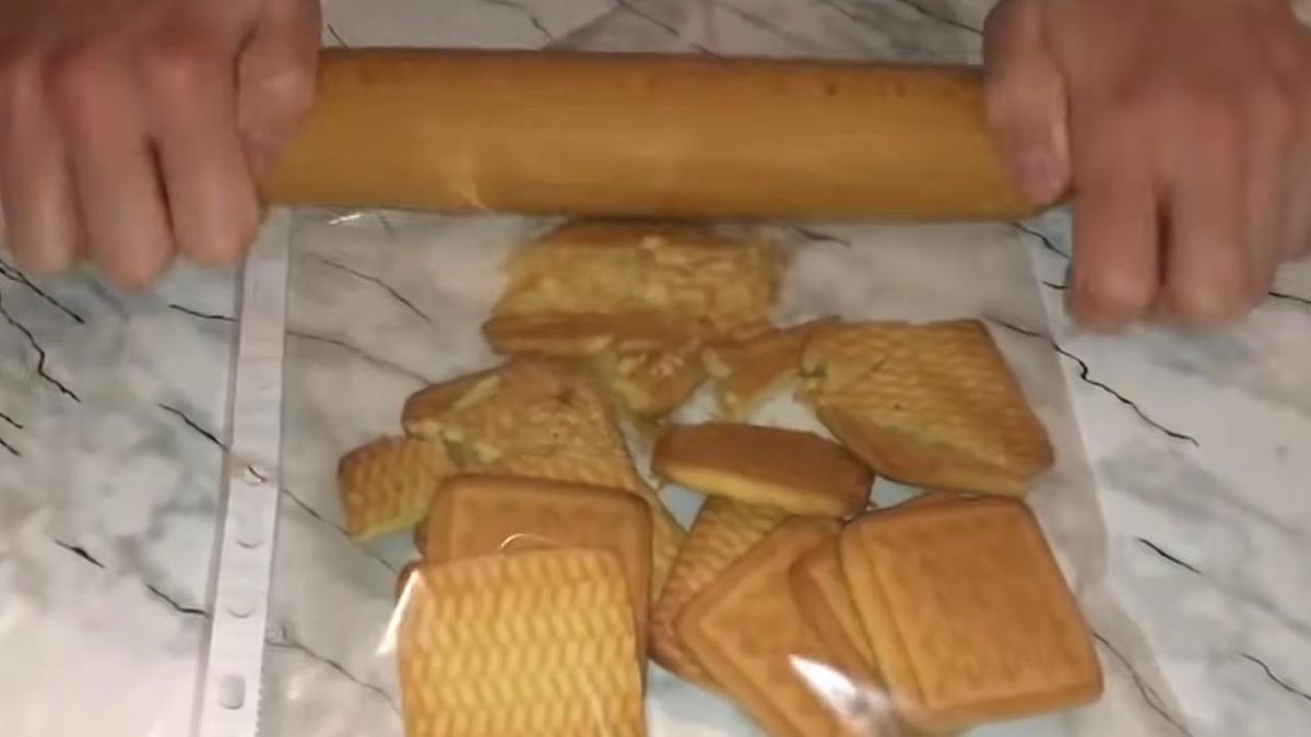 На столе пакет с печеньем, которое измельчают в крошку скалкой