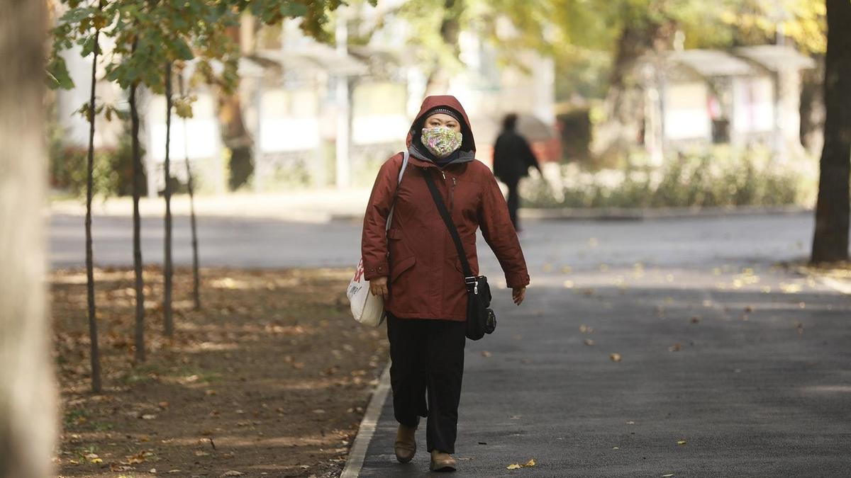 Женщина в куртке и маске идет по улице