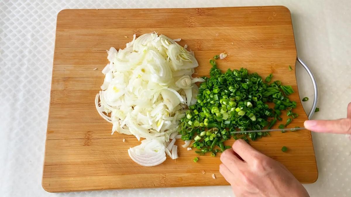 На разделочной доске нарезают репчатый и зеленый лук