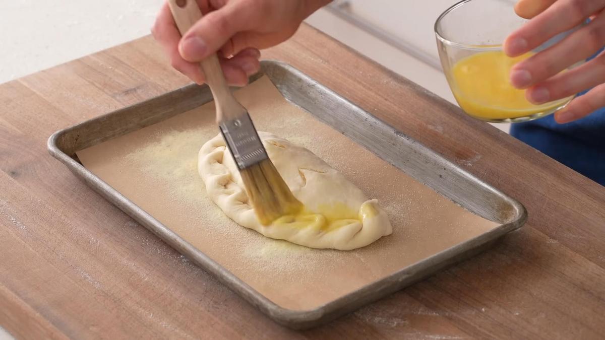 Кальцоне на противне смазывают яйцом