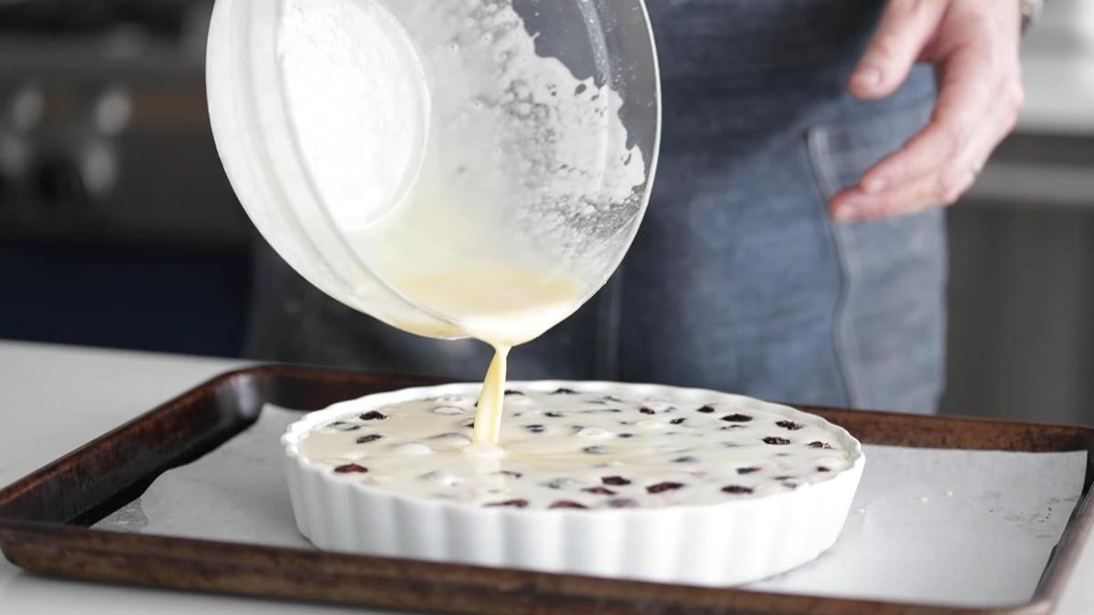 Мужчина выливает тесто из стеклянной миски в керамическую форму с вишнями