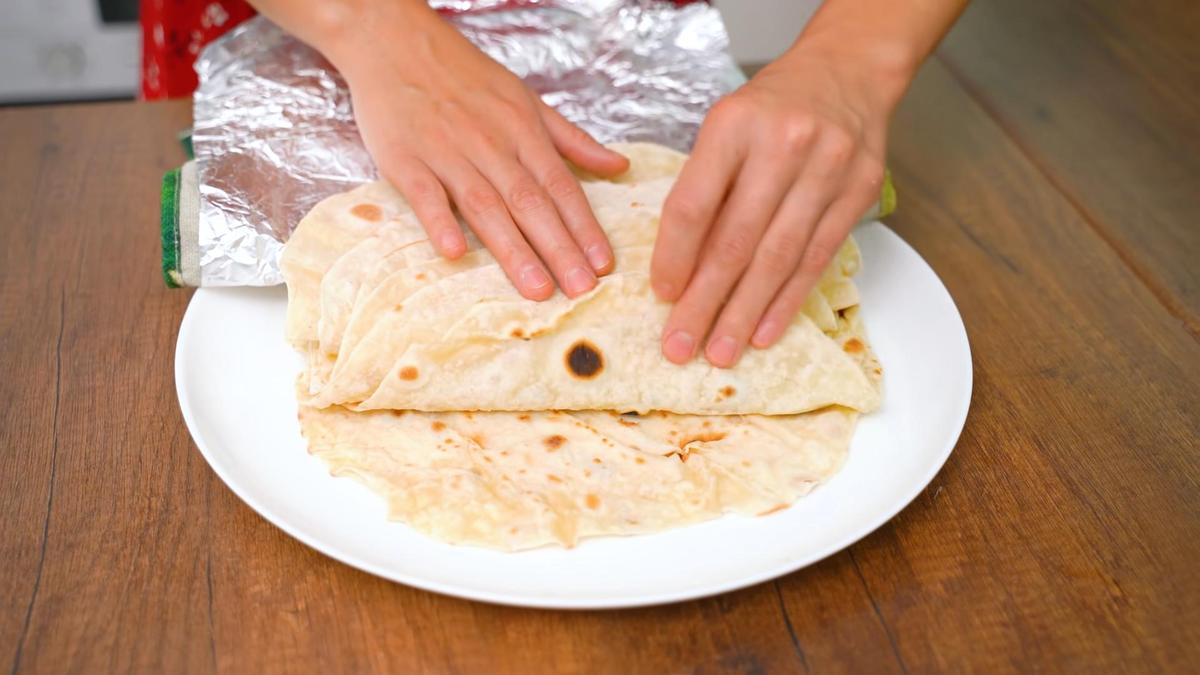 Женские руки держат стопку лавашей, накрытых фольгой