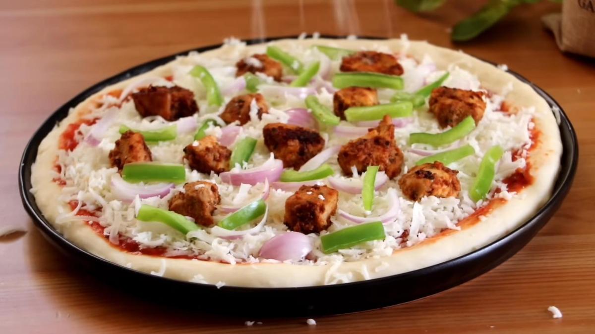 Пиццу с начинкой из курицы, перца и лука посыпают сыром