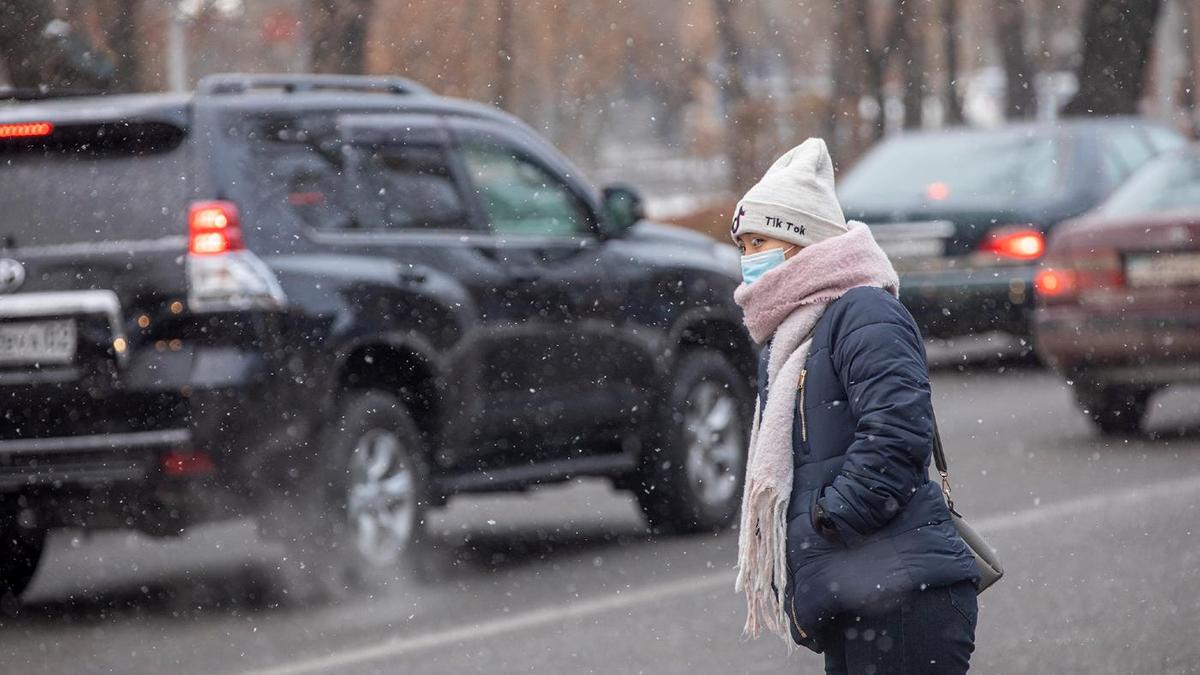 Женщина в маске стоит около проезжей части