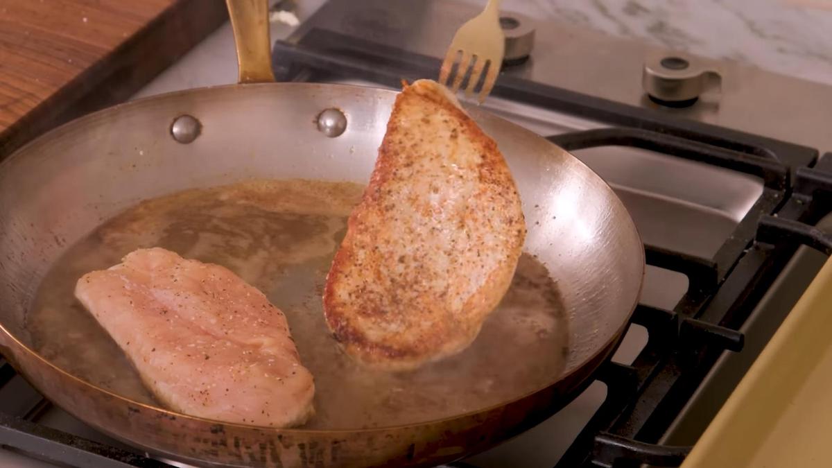 На сковороде вилкой переворачивают поджаренное филе