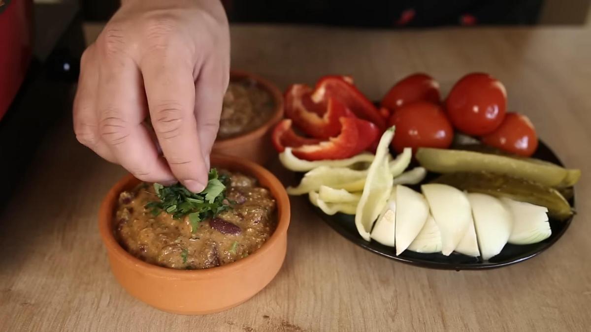 Лобио посыпают нарезанной кинзой. Рядом тарелка с соленьями