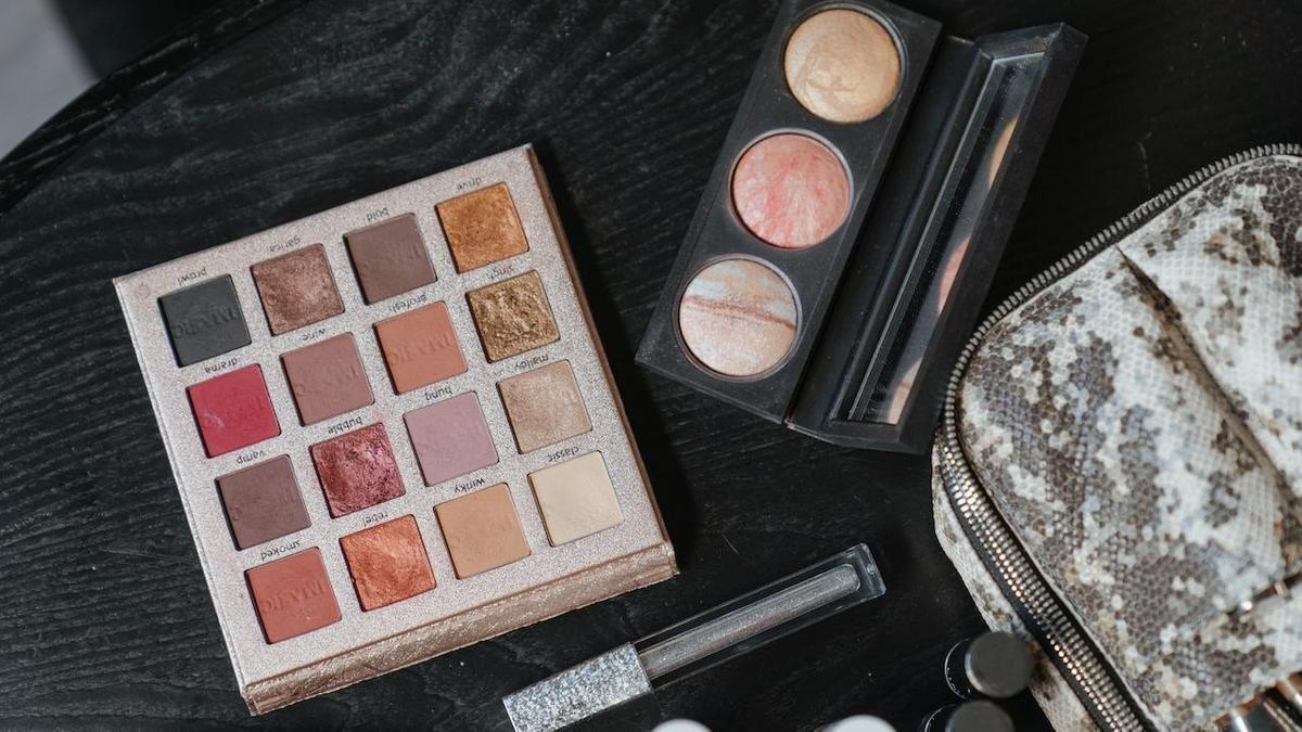 Палетка теней, хайлайтер, жидкие тени, косметичка лежат на столе