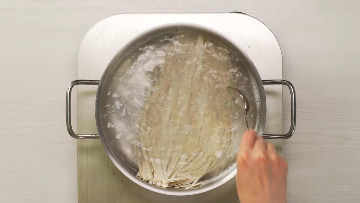 Лапшу удон перемешивают ложкой в кипящей воде