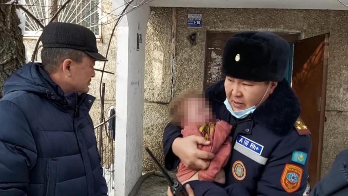 Спасатель держит на руках маленького ребенка у подъезда жилого дома Спасатель держит на руках маленького ребенка у подъезда жилого дома