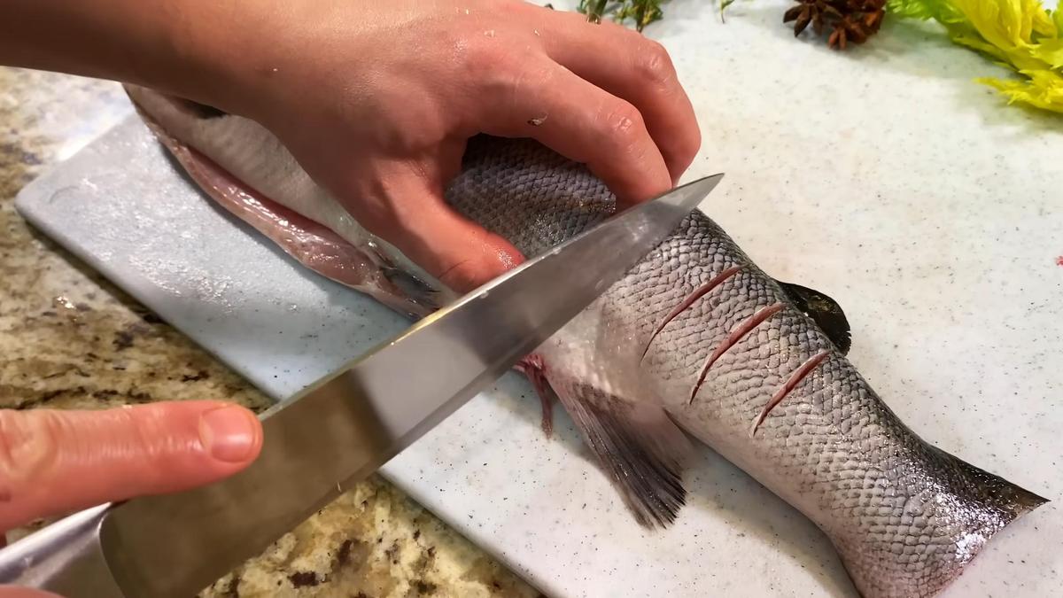 На разделочной доске свежая форель, на которой делают надрезы ножом