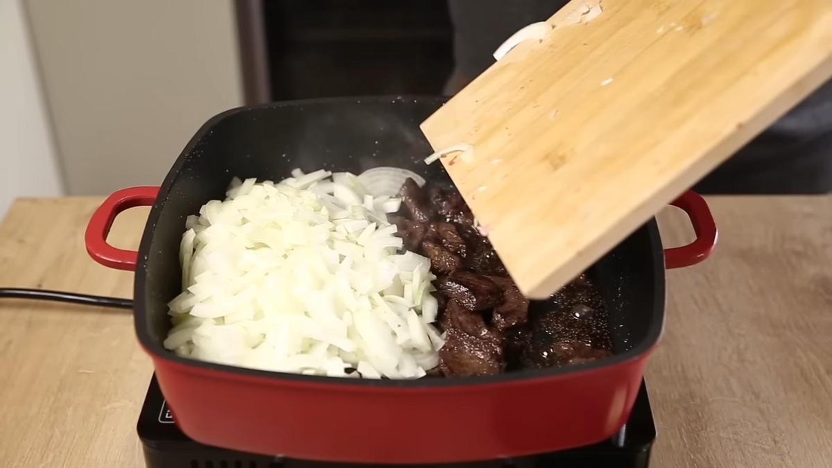 Лук перекладывают в сковороду с мясом с разделочной доски