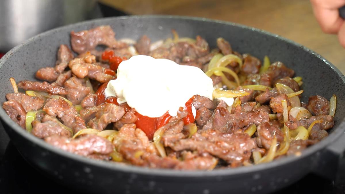 На сковороде мясо с луком, кетчупом и сметаной