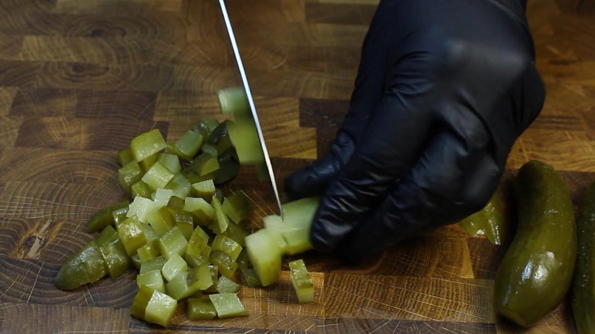 На разделочной доске нарезают маринованные огурцы