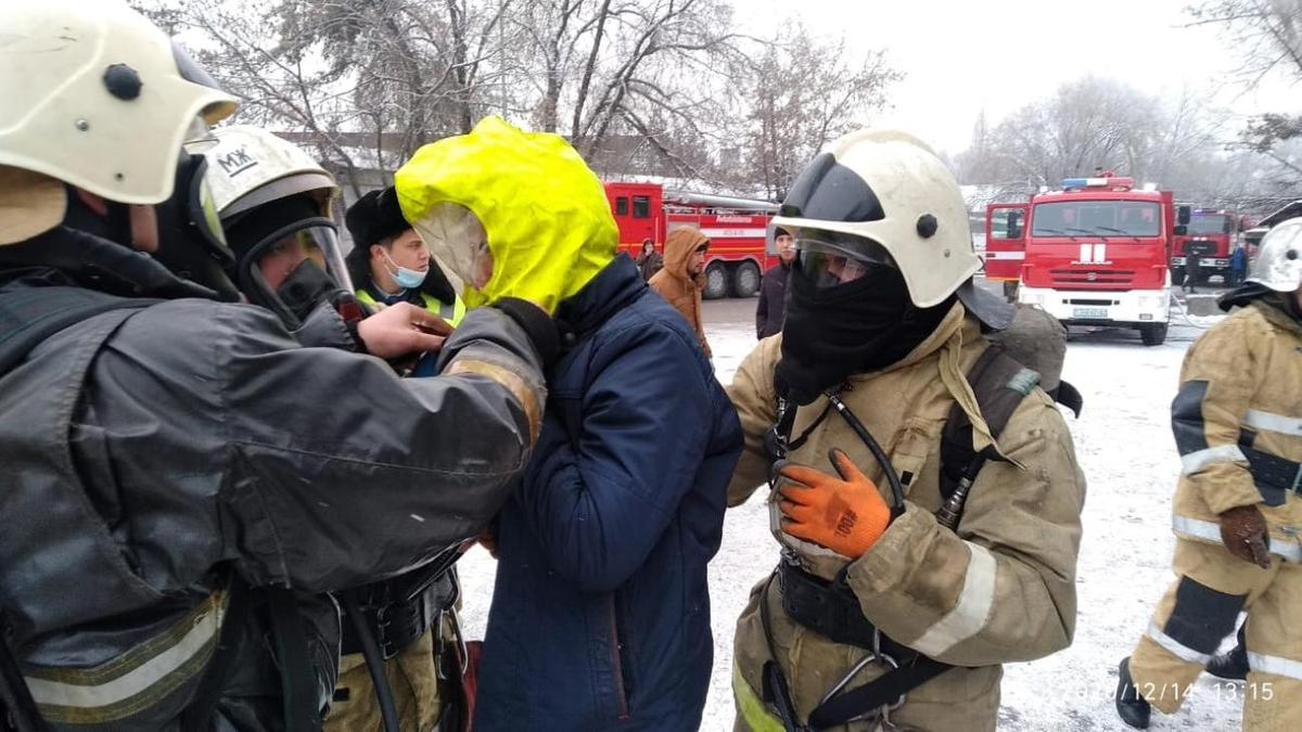 Пожарные стоят вокруг мужчины на фоне спецтехники