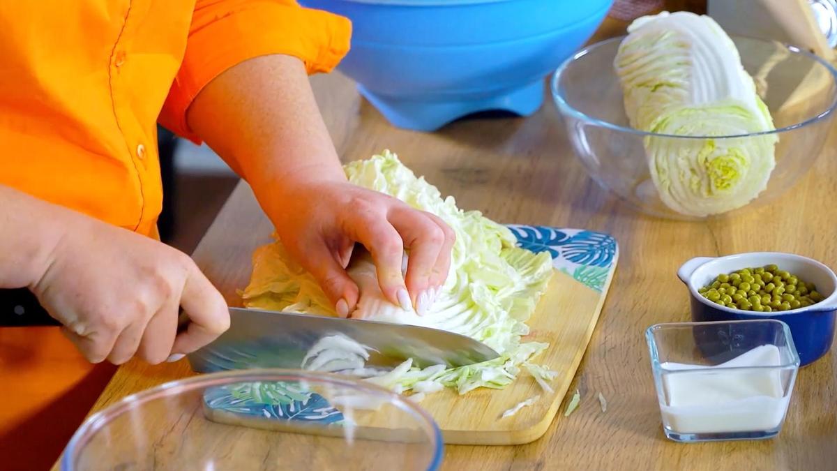 На разделочной доске ножом шинкуют листья пекинской капусты