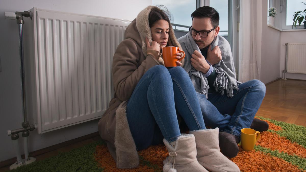 Мужчина и женщина в теплой одежде сидят у батареи