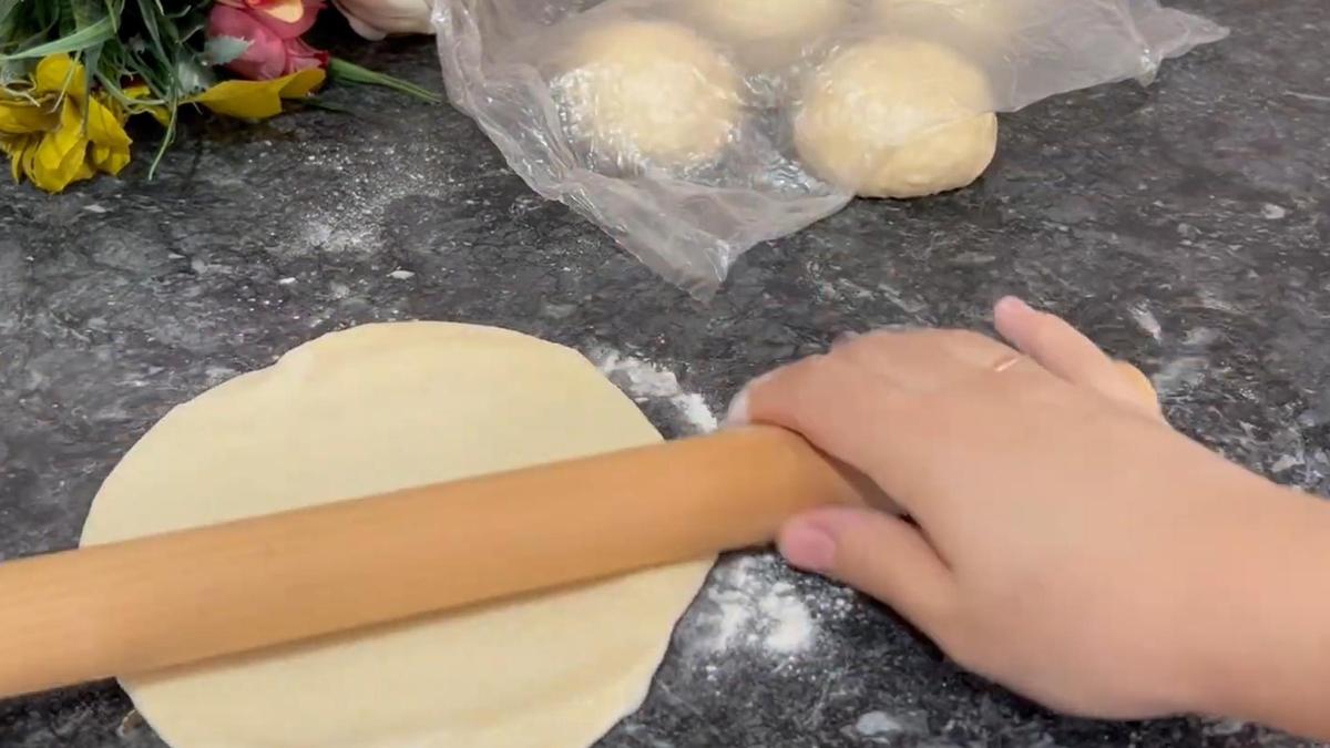 На столе раскатывают тесто скалкой