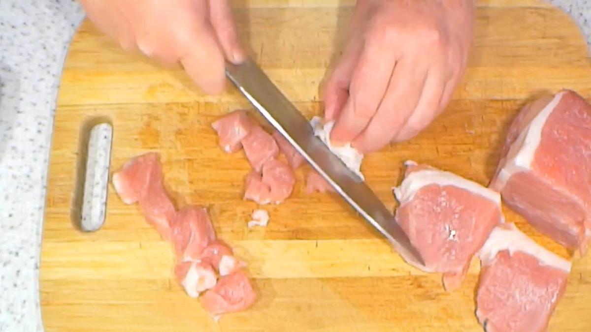 На разделочной доске нарезают свинину на кусочки
