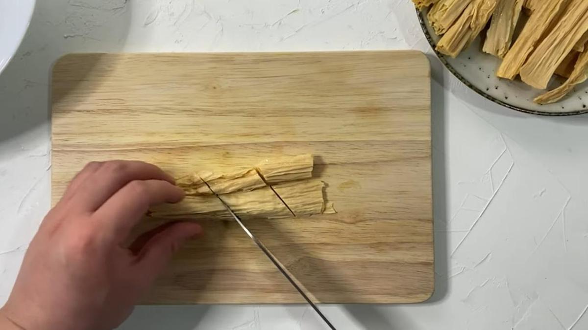 Соевую спаржу нарезают на разделочной доске