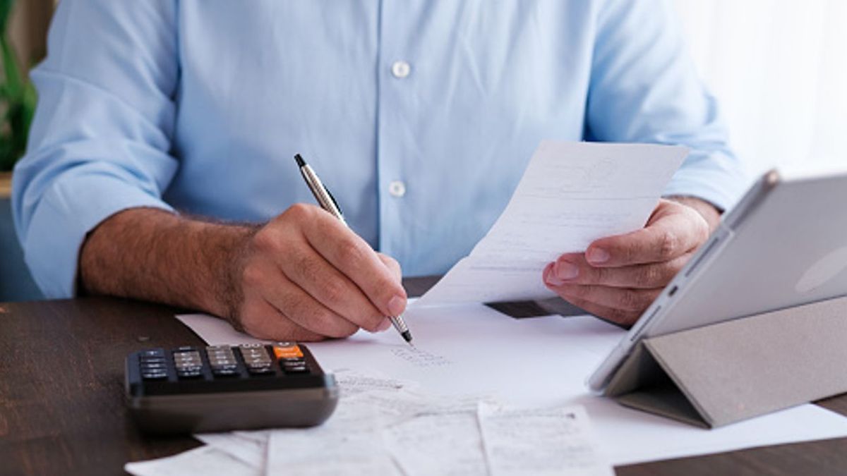 Мужчина держит счет, ручку, перед ним чеки, калькулятор и планшет