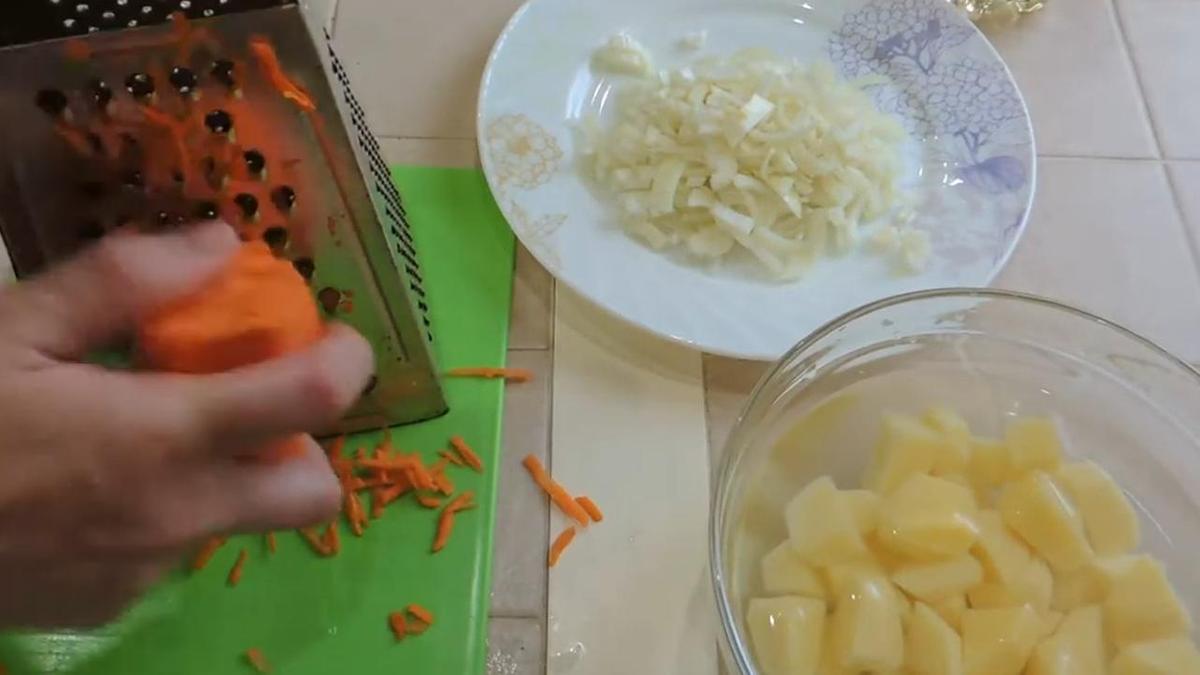 Морковь натирают на терке. Рядом тарелка с картофелем и нарезанным луком
