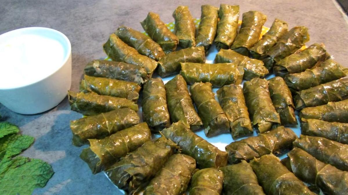 Готовая долма на сервировочной тарелке рядом со сметанным соусом