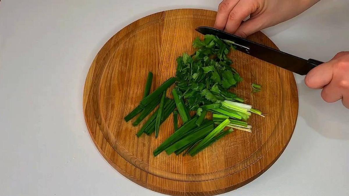 На разделочной доске нарезают зеленый лук