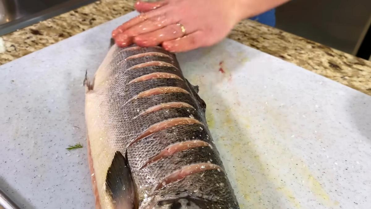 На разделочной доске свежая форель, которую смазывают маслом