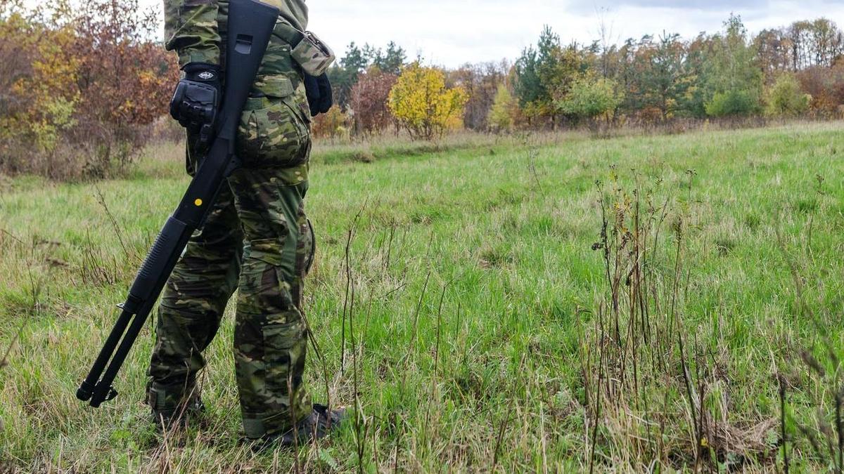 Мужчина с оружием стоит в поле