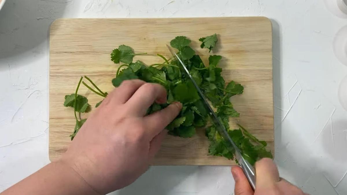Кинзу нарезают на разделочной доске