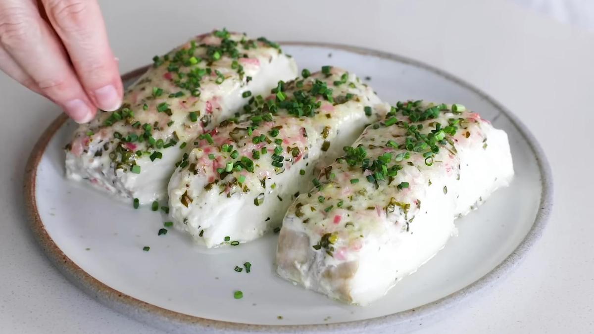 На тарелке запеченные куски филе палтуса, которые посыпают нарезанным шнитт-луком