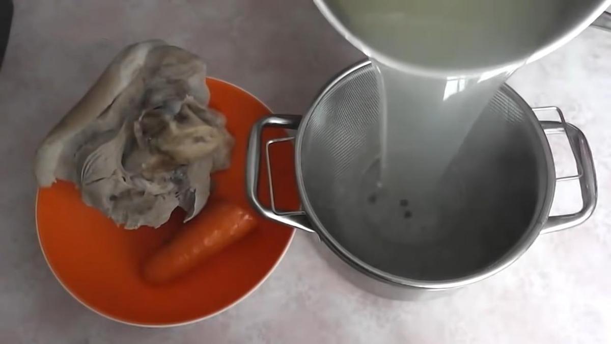 На тарелке мясо и морковь. Рядом кастрюля с ситом, через которое сливают бульон