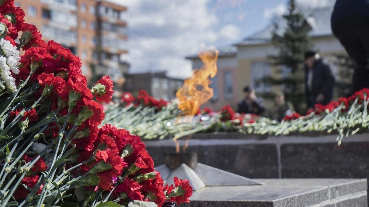 Охапки гвоздик лежат возле горящего Вечного огня