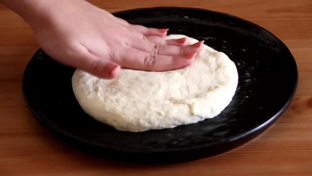 Тесто разминают руками, формируя основу для пиццы