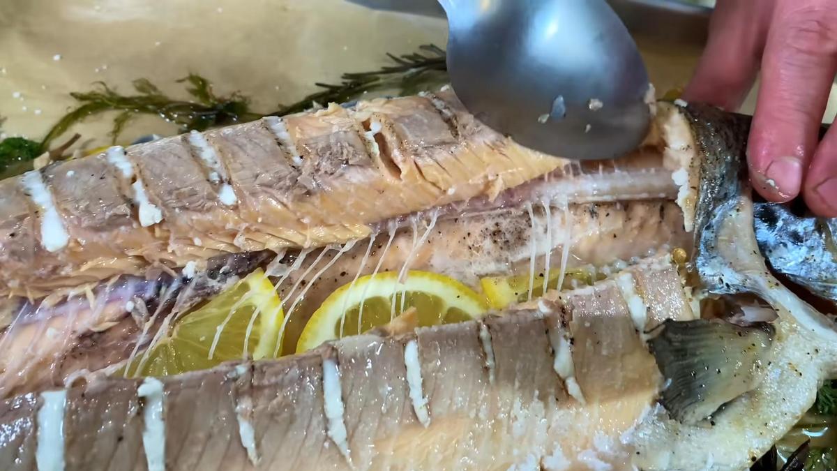 Ложкой отделяют запеченное мясо форели от хребта и костей