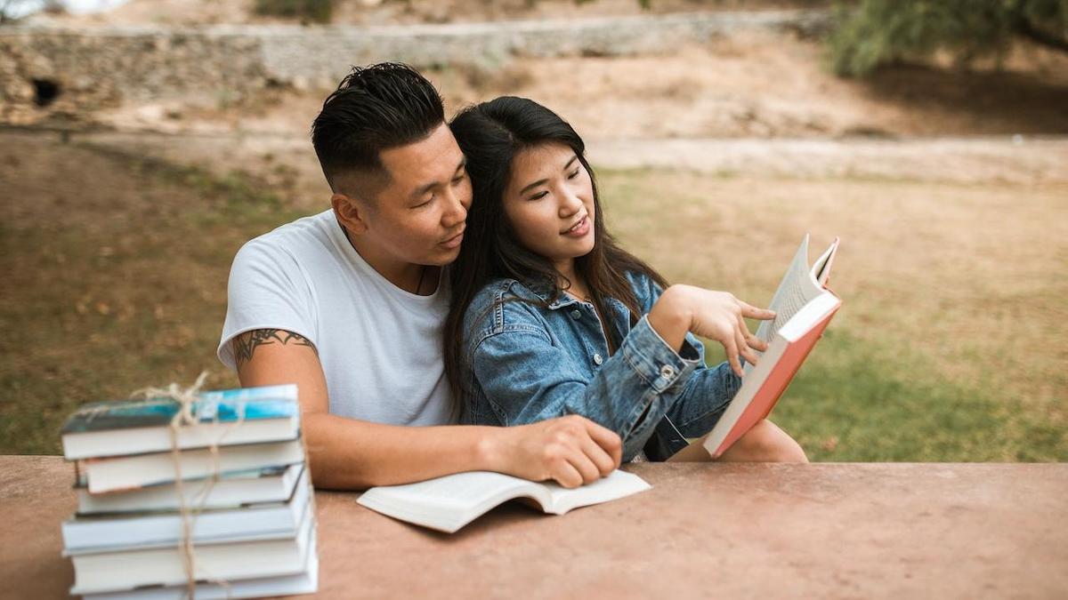 Влюбленная пара читает книгу рядом со столом, на котором лежит стопка книг