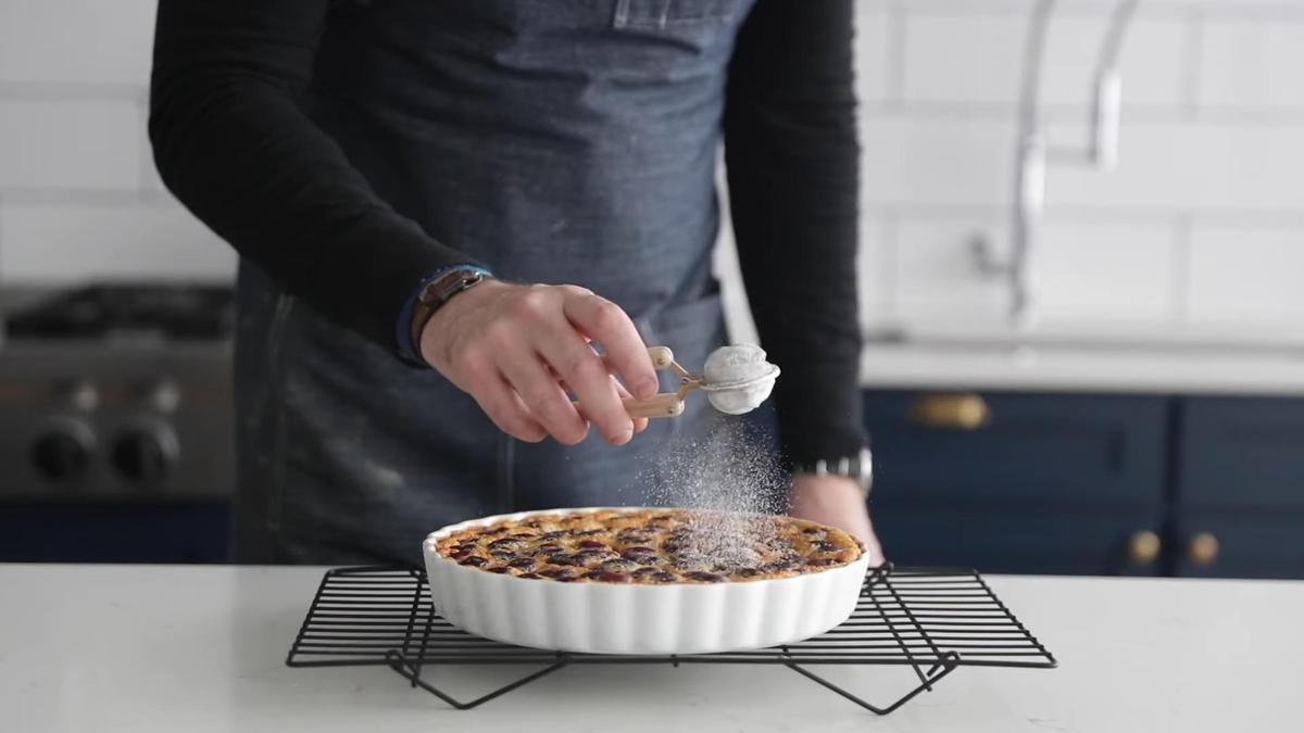 Мужчина посыпает испеченный клафути сахарной пудрой