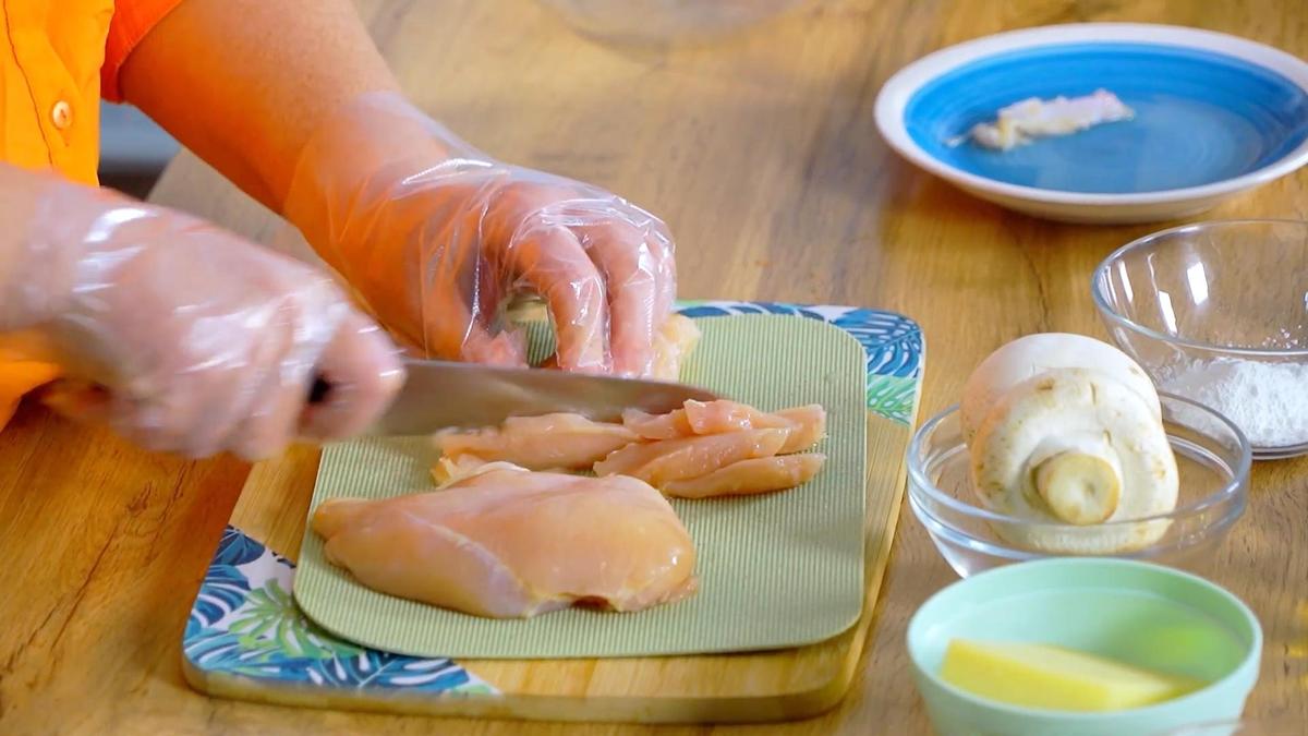 Куриное филе нарезают на тонкие ломтики на разделочной доске