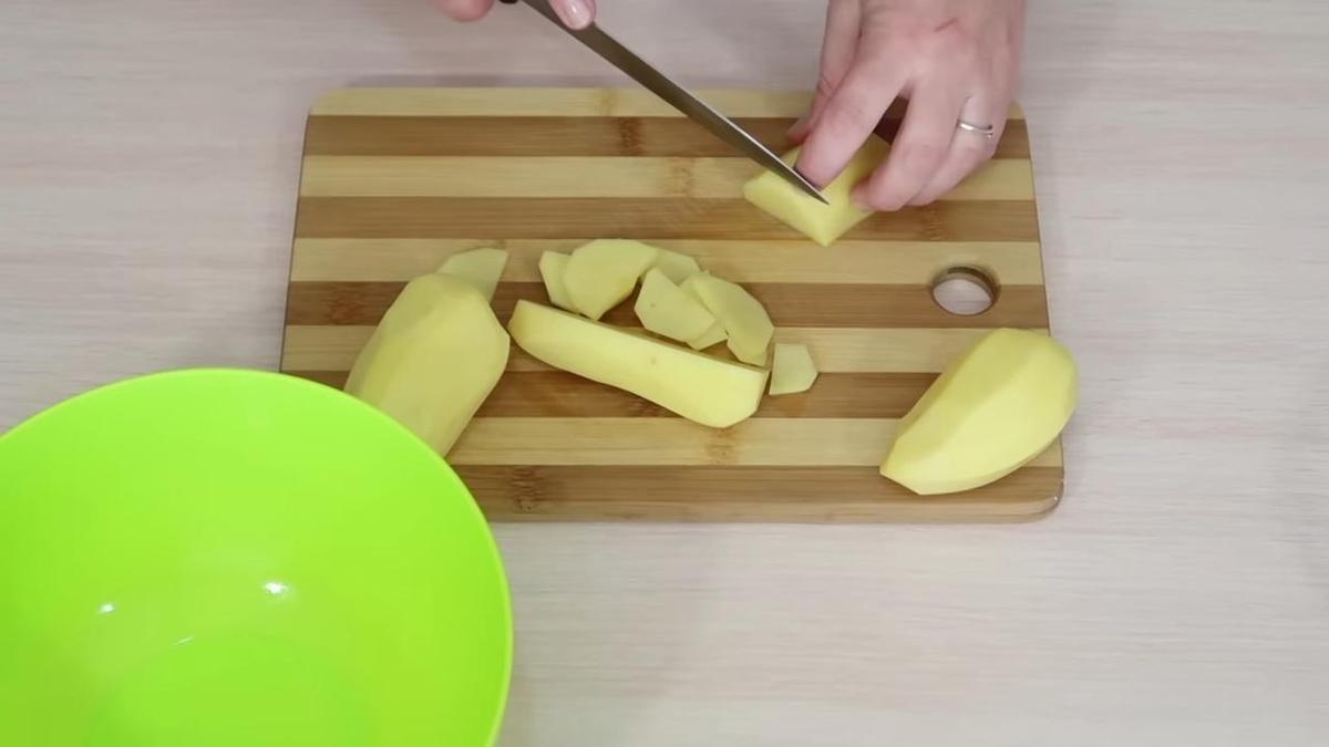 На разделочной доске ножом нарезают картофель на слайсы