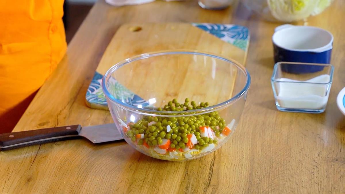 В стеклянном салатнике крабовые палочки, нарезанные яйца и горошек