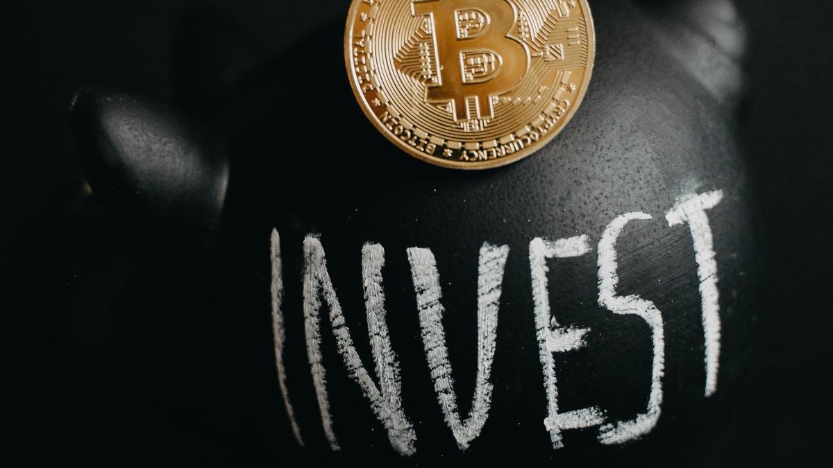 Монета биткоина на фоне копилки с надписью INVEST