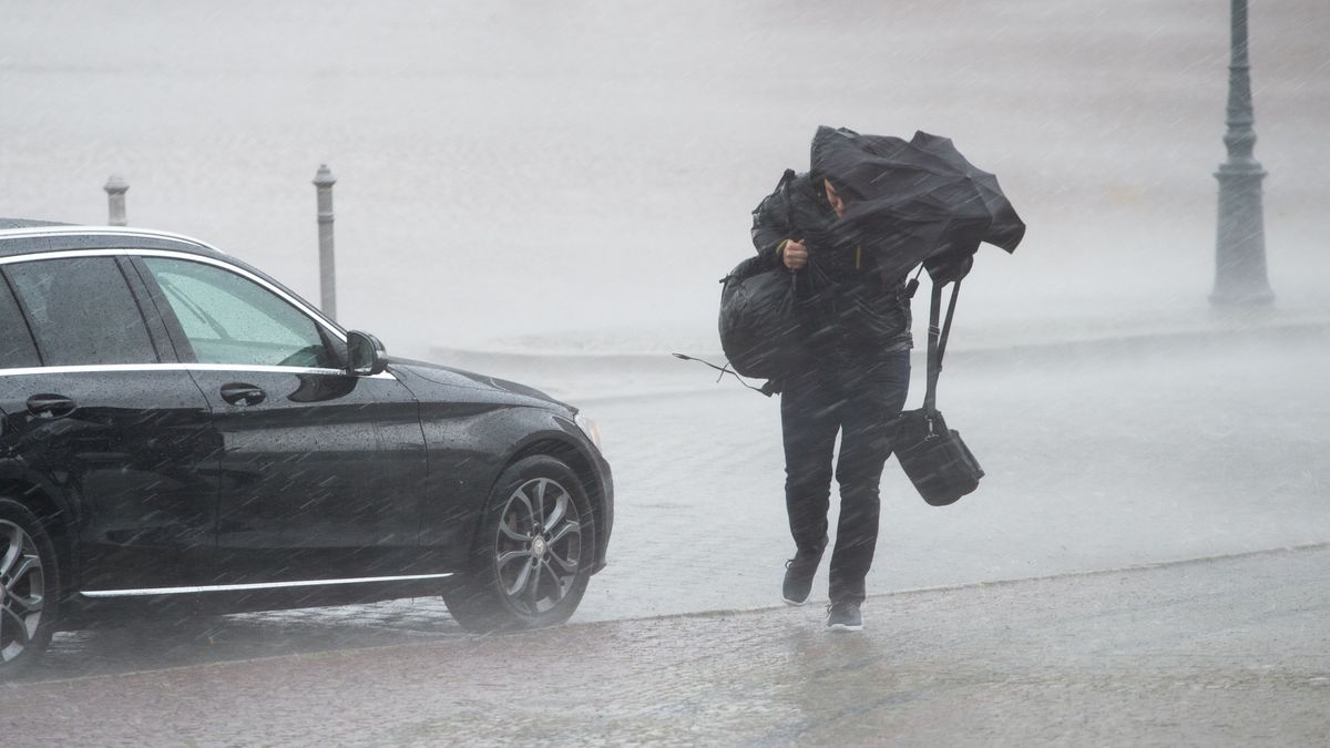 Мужчина прикрывается зонтом от дождя и ветра