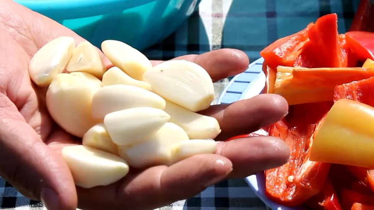 В руках очищенные зубчики чеснока, рядом сладкий перец