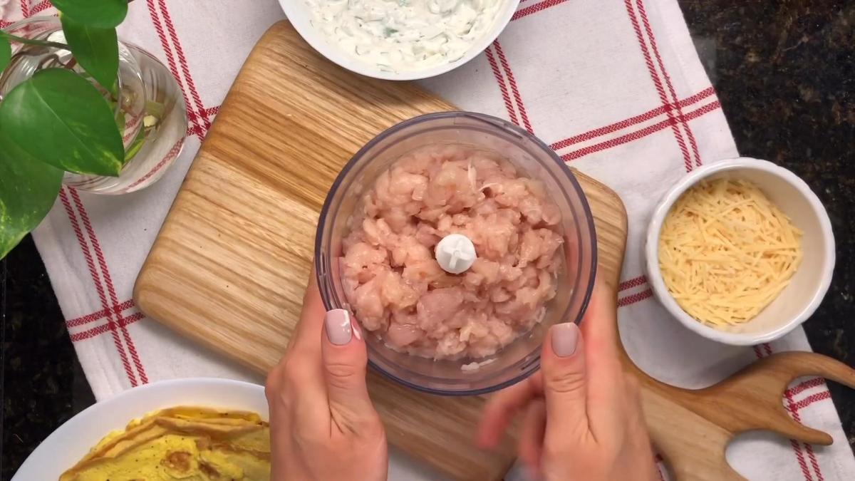 Девушка держит в руках чашу блендера с нарезанным куриным филе