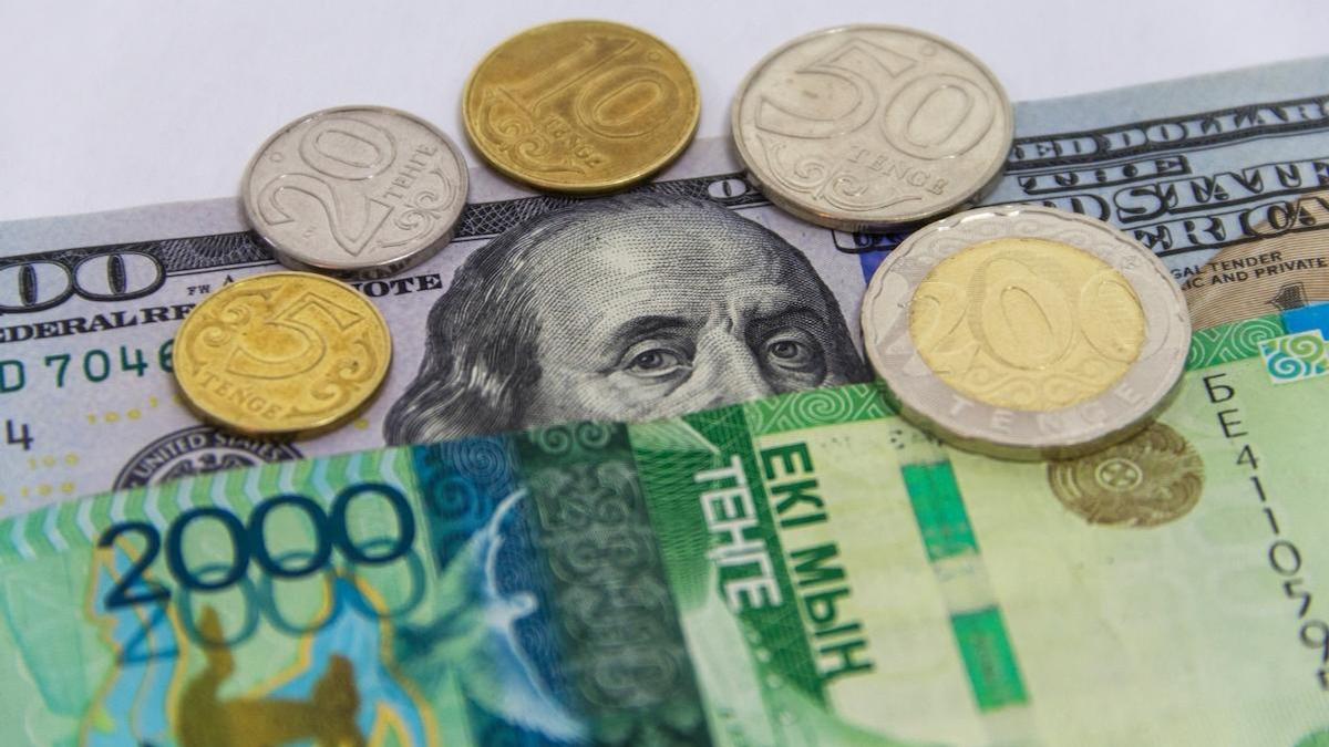 Монеты и купюры тенге лежат на долларовой банкноте