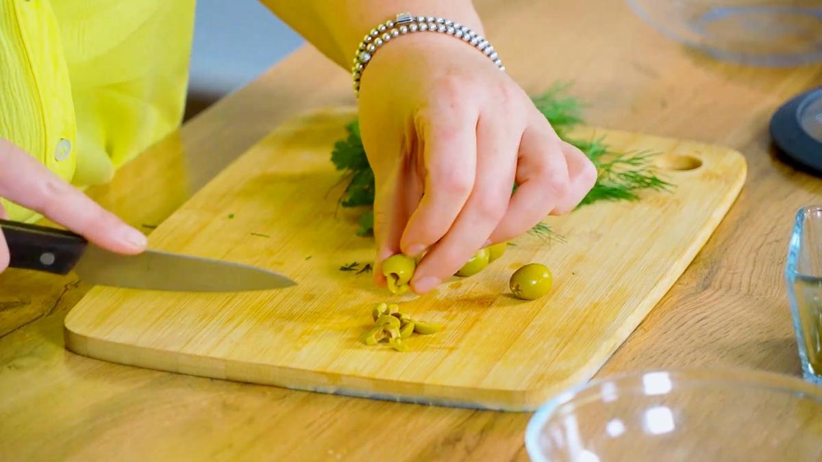 Зеленые оливки нарезают на разделочной доске